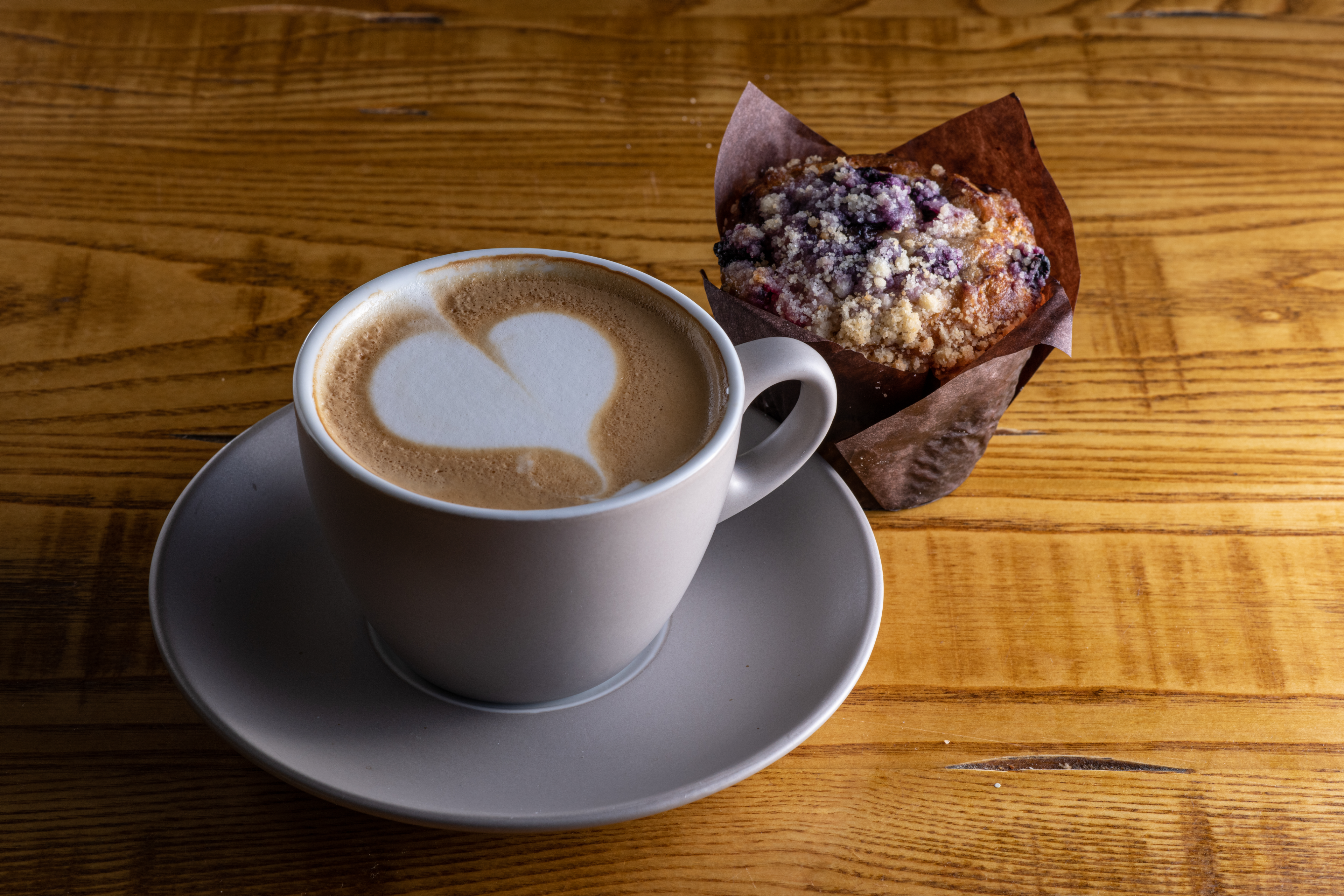 A hot beverage with latte heart and a blueberry muffin