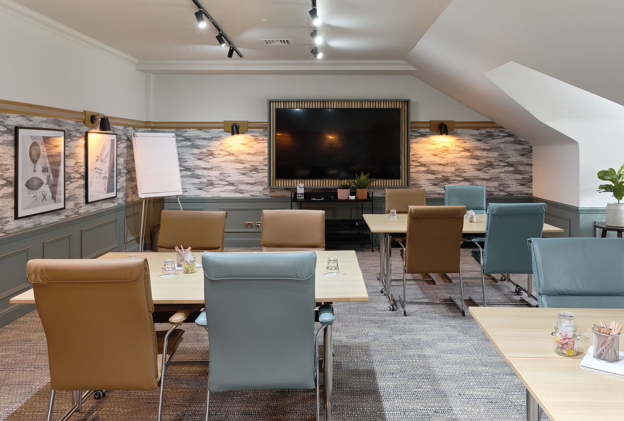 A meeting room equipped with four-person tables, a flip chart and a screen